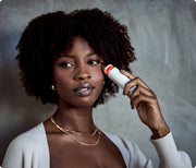 Woman using the white Therabody TheraFace Depuffing Wand with heat setting on her under eye