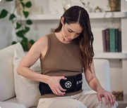 Woman adjusting the controls of the Therabody ThermBack LED while sitting on the sofa