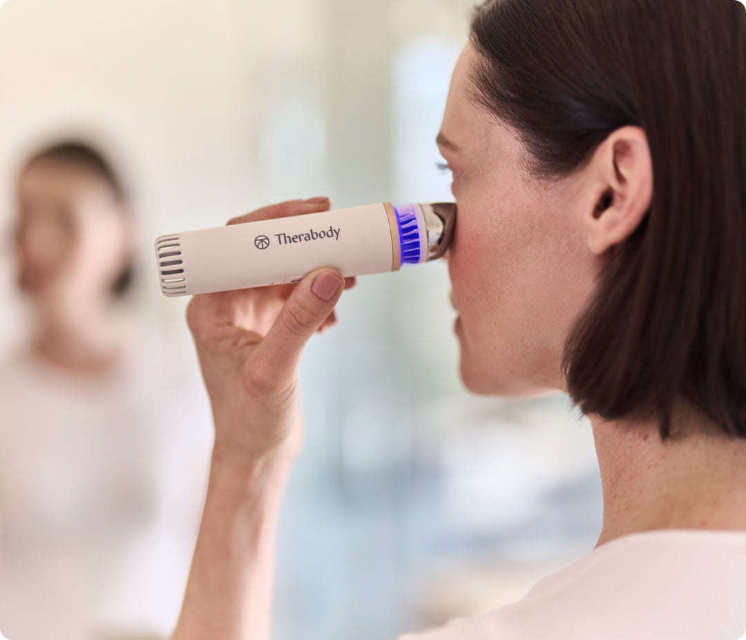 Woman using the white Therabody TheraFace Depuffing Wand on its cold setting on her under eyes while looking in the mirror