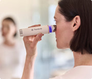 Woman using the white Therabody TheraFace Depuffing Wand on its cold setting on her under eyes while looking in the mirror