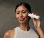 Load image into Gallery viewer, Woman using the Therabody TheraFace Depuffing Wand in white on her cheekbones