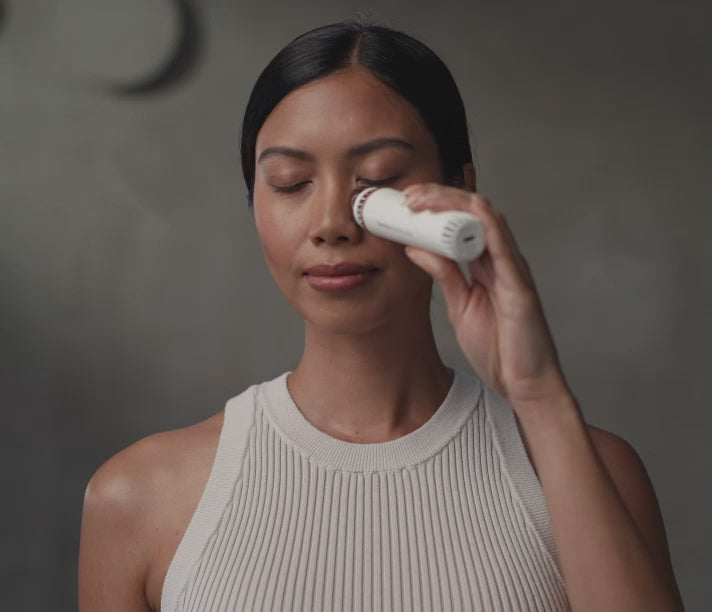 Woman using the white Therabody TheraFace Depuffing Wand on her face